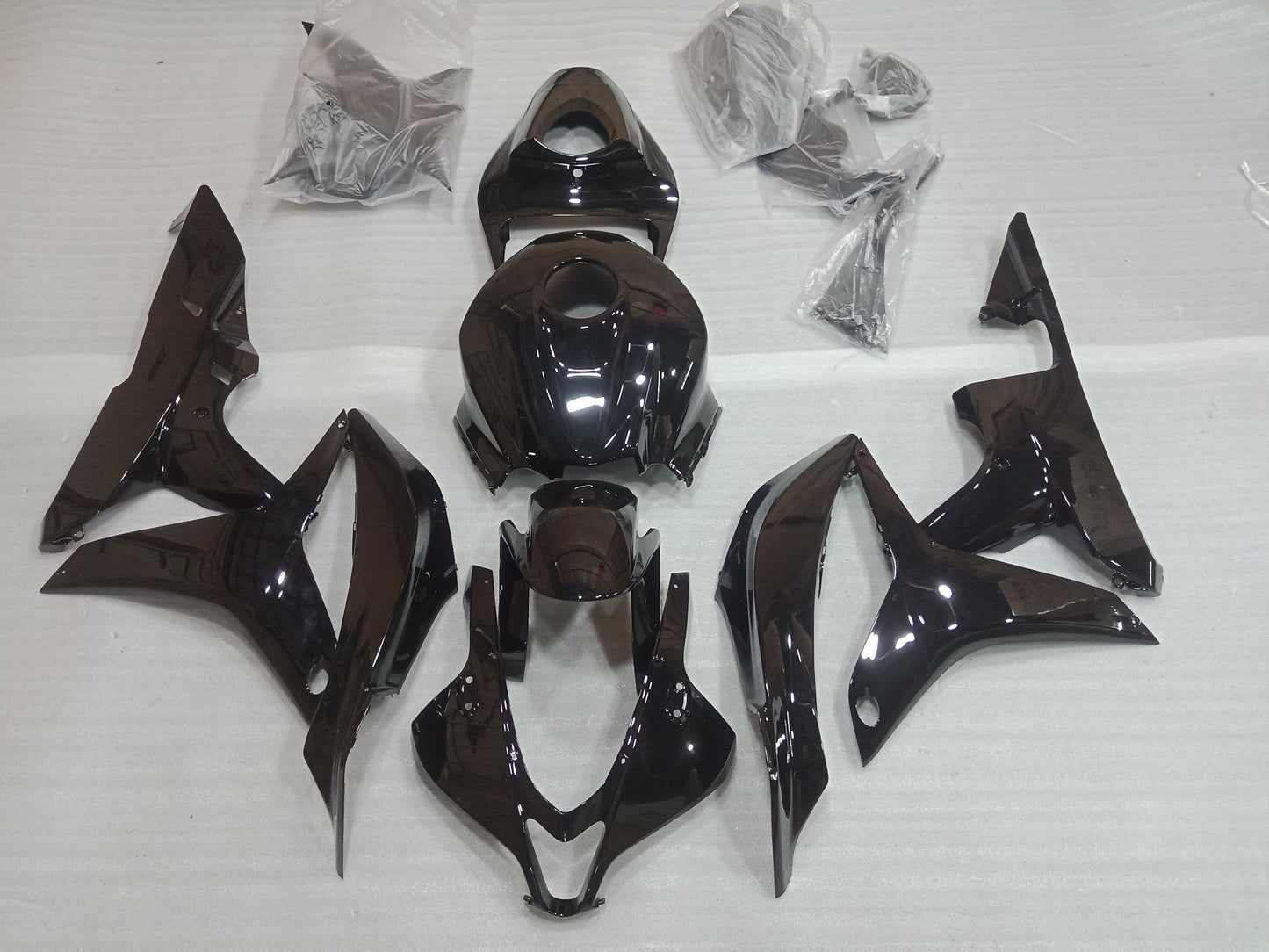 A set of gloss black motorcycle fairings laid out on a white surface, including various panels and bolts, for a Honda CBR600RR.